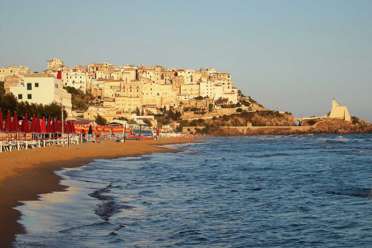 Scorcio panoramico di una delle spiagge dorate di Sperlonga, con acqua trasparente, ombrelloni colorati e il borgo bianco sullo sfondo