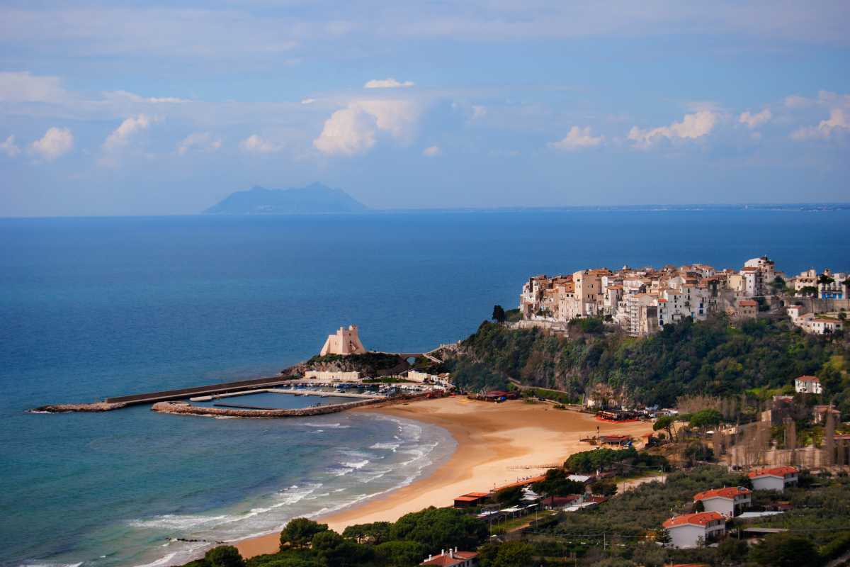 Vista ravvicinata della Spiaggia della Grotta di Tiberio a Sperlonga: ciottoli, acqua trasparente, grotta sullo sfondo, persone che fanno snorkeling